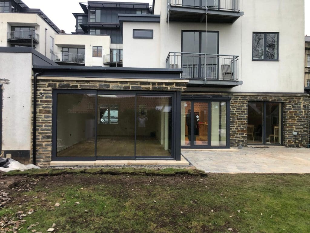 Modern stone and white new build with large glass sliding doors facing a lawn