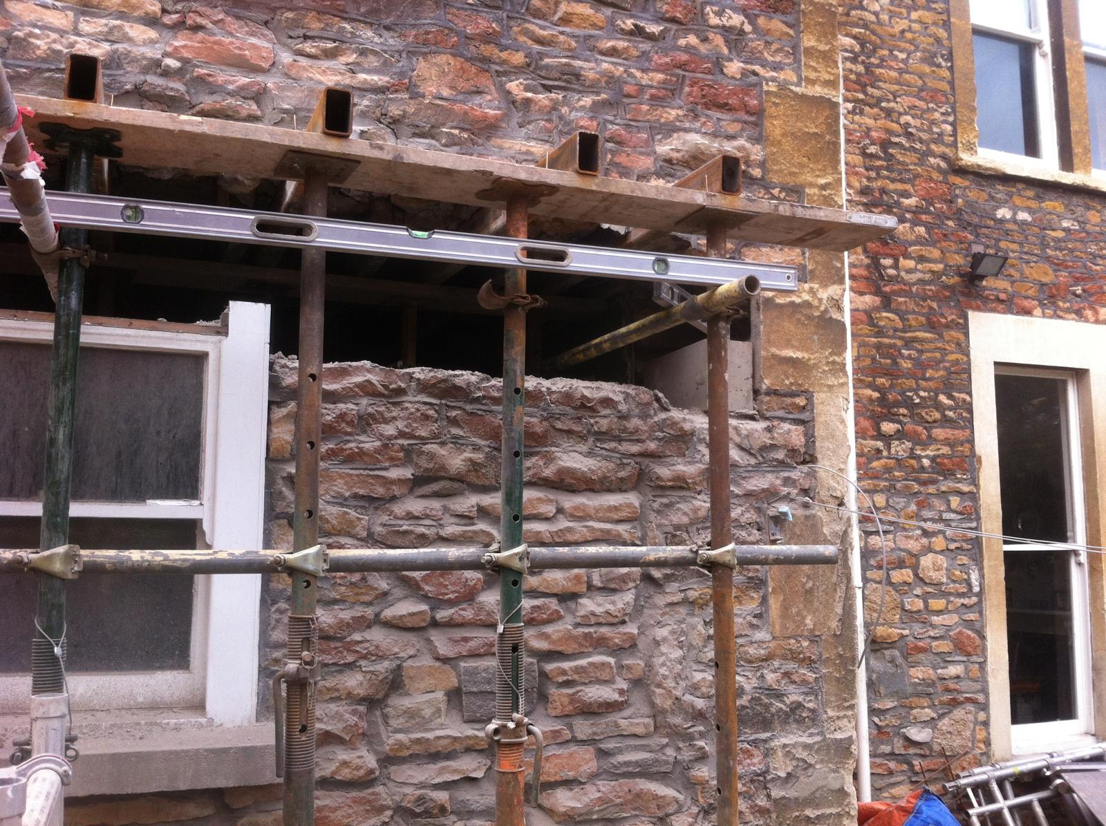 Scaffolding and a spirit level against a Bristol stone wall being extended by RSJ Construction