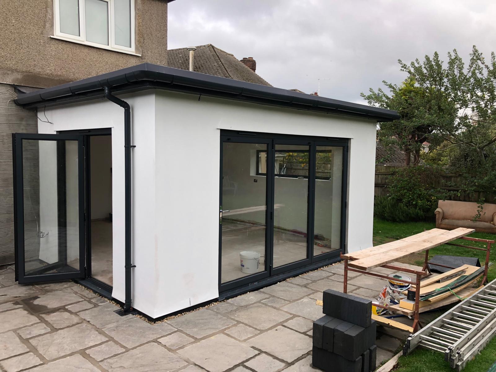 Newly built white house extension with large glass doors opening onto a stone patio